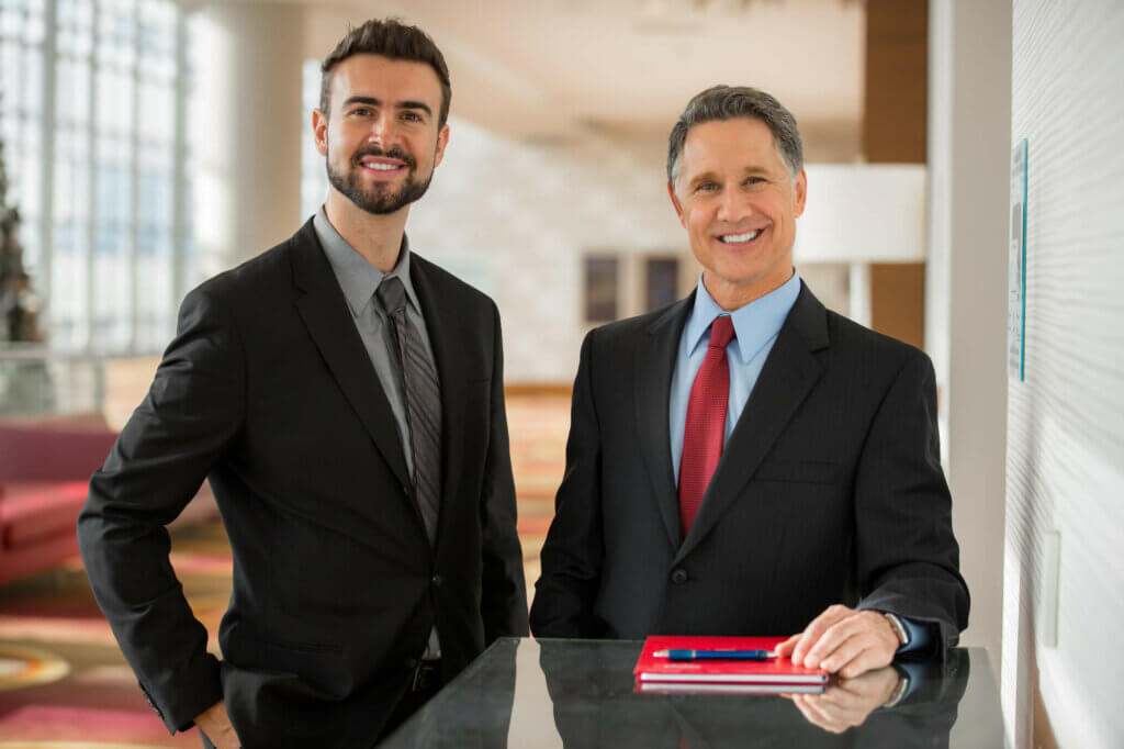 Zwei Businessmänner lachen in die Kamera mit rotem Notizbuch